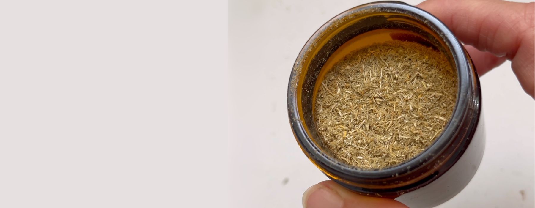 Hand holding brown glass jar with herbal styptic powder.